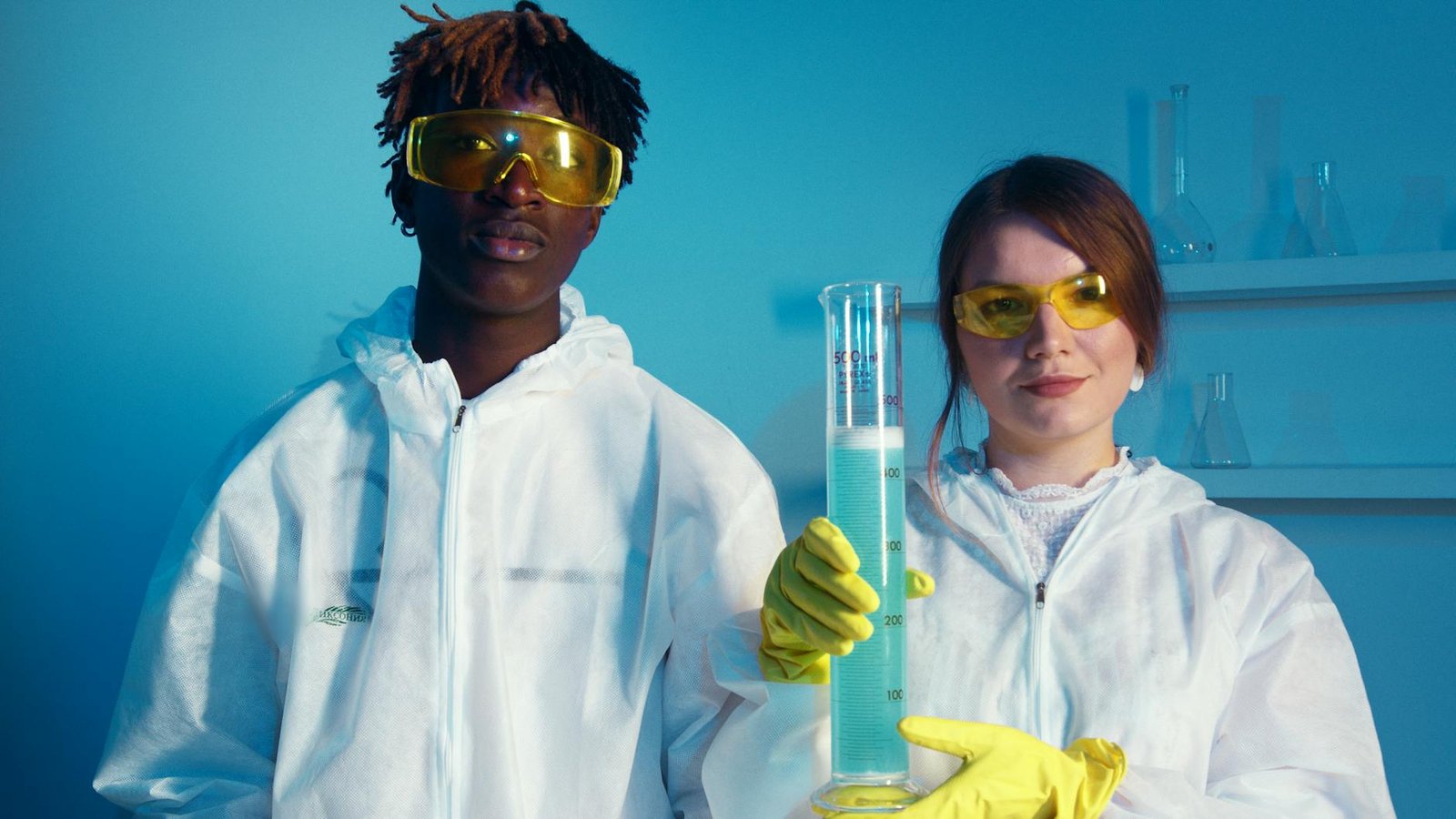 a man and a woman looking at the camera while holding a big graduated cylinder